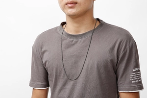Detail of a thin black stainless steel O-chain necklace worn by a male model