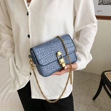 Détail du sac en cuir bleu à motif crocodile avec chaîne dorée sur tenue blanche