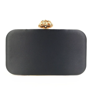 Detail of elegant black satin evening clutch featuring a gold floral metal clasp closure