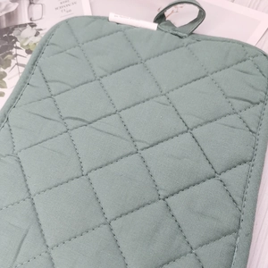 Detail of sage green quilted cotton insulation pad with diamond stitching and a hanging loop