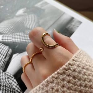 Close-up of minimalist gold layered rings set on a model with beige knitwear background