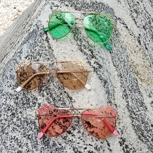Daisy flower kids aviator sunglasses in green, brown, and pink on stone background