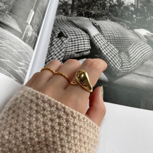 Close-up of a high-polished golden teardrop ring on finger with a cozy knit background