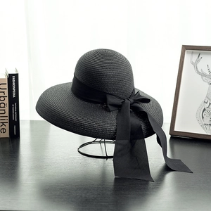 Elegant black straw sun hat with long bow ribbon on metal stand for summer beach trips