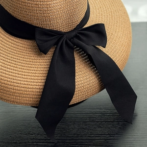 Close-up of the woven straw texture and elegant black bow on the khaki sun hat