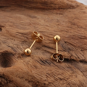 Macro view of minimalist gold bead stud earrings on a dark textured wood surface