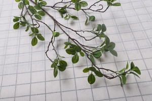 Detailed view of artificial Milan leaves on dark brown stems against a grid backdrop