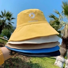 Dettaglio di cappelli da sole in cotone colorati impilati sull'erba con ricami a margherita
