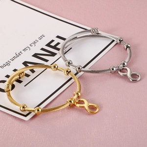Infinity charm cable wire bracelets in gold and silver finish on a pink background