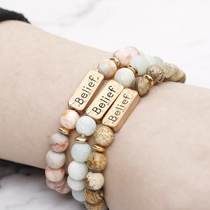 Three beaded natural stone bracelets with gold metal bar engraved with Belief on marble background