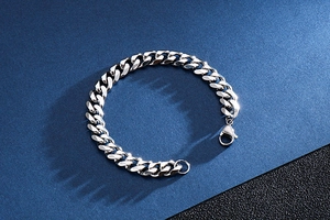 Macro shot of silver stainless steel Cuban link bracelet with lobster clasp on blue background