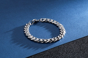 Macro detail of high-polish silver stainless steel Cuban chain bracelet on blue surface