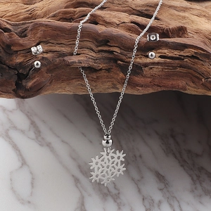 Close-up of silver hollow snowflake pendant necklace and earrings on wood and marble