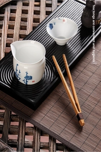 Close-up of bamboo tea tongs with blue floral ceramic cups on a traditional tea tray