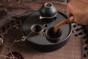 Detail of matte black ceramic tea set with wooden spoon being used in a zen tea ceremony