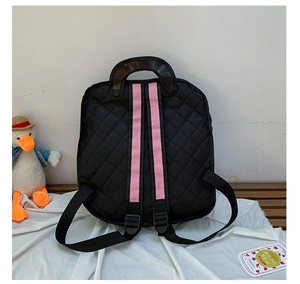 Quilted black 2D backpack for women with pink straps and brown handle on a white stool