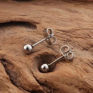 Minimalist silver steel ball stud earrings pair with backings on wooden surface