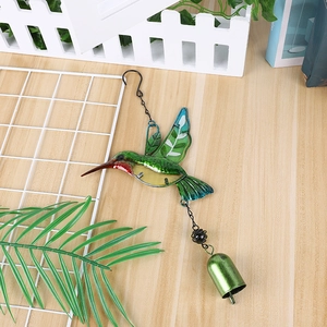 Macro shot of colorful glass hummingbird wind chime with green metal bell on wood surface