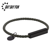 Detail view of woven dark green cord bracelet with black matte metal bar and small charm tag