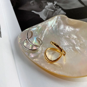 Close-up of minimalist silver and gold irregular twist rings on a pearl shell tray