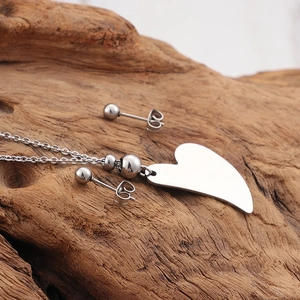 Polished heart pendant necklace and ball stud earrings set on a textured wooden base