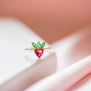 Gold strawberry ring with red heart gemstone and green leaf accents on pink silk
