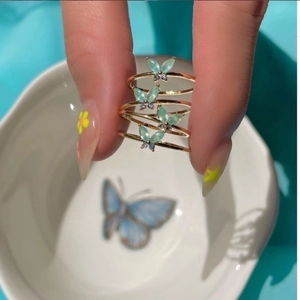 Macro shot of a layered gold ring featuring green butterfly charms with clear gemstones