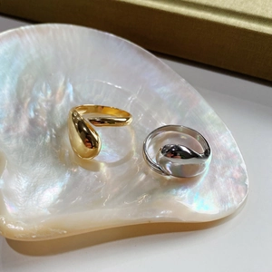 Detail view of teardrop open rings in gold and silver finish on iridescent shell tray