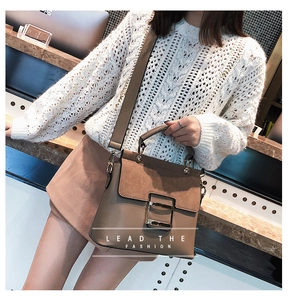 Detail of a brown crossbody bag featuring matte leather texture and a large gold metal buckle