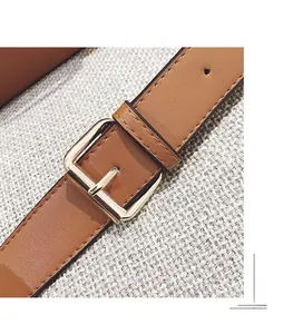 Detail of brown leather strap with polished gold rectangular buckle and neat stitching