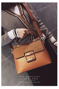 Close-up of brown textured leather crossbody bag with square gold buckle on model