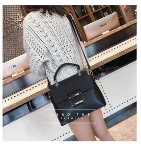Fashionable black faux leather crossbody bag with a large gold buckle on a shop background