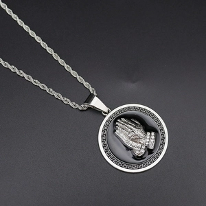 Macro detail of silver prayer hands pendant with greek fret pattern on twist chain