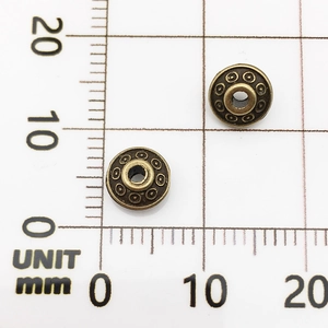 Detail view of 8mm bronze alloy spacer beads showing dot texture and size on scale paper