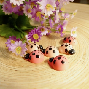 Detailed view of pink and cream resin ladybug charms for DIY crafts on a wooden tray