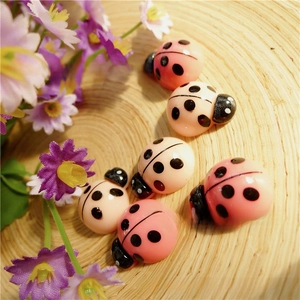 Macro shot of cute resin ladybug DIY charms in pink and cream on a wooden tray