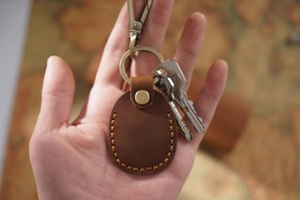 Handheld view of a brown genuine leather keychain case with vintage map backdrop
