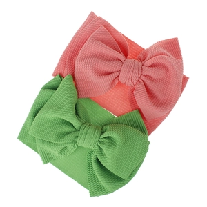 Macro detail of two soft waffle fabric baby headbands with oversized bows in pink and green