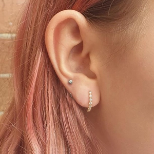 Macro view of gold hoop earring with white zircons on model with pink hair