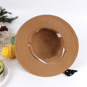 Detailed close-up of brown straw sun hat featuring a polka dot bow and inner elastic strap