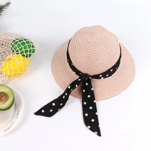 Detail of pink woven straw sun hat featuring a black and white polka dot ribbon bow