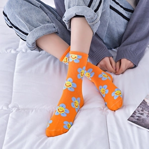 Orange cotton crew socks with blue flowers and yellow smiley faces on white bedding