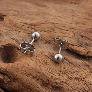 Macro shot of polished silver ball stud earrings with butterfly backs on a rustic wood base