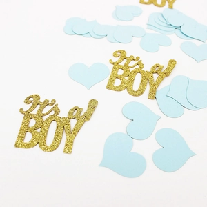 Close-up of golden glitter 'It's a BOY' letters and light blue heart-shaped confetti