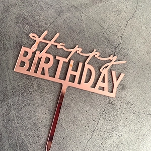 Rose gold acrylic Happy Birthday cake topper with mirror finish on grey background