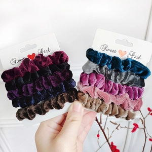 Set of six velvet scrunchies in assorted colors held by hand against white background