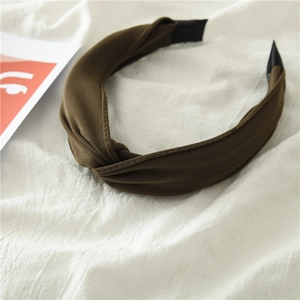 Detail of a dark brown knotted fabric headband on soft white linen background