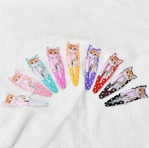 Macro shot of colorful cat-shaped metal hair clips in nine shades on white fabric