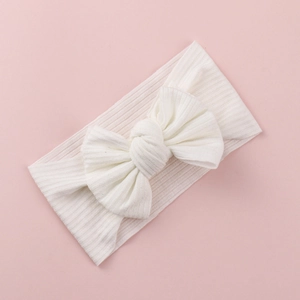 Close-up of white knitted baby headband with a large bow on a soft pink background