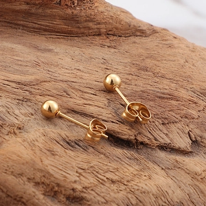 Minimalist golden round stud earrings on a textured wooden background with butterfly clasp